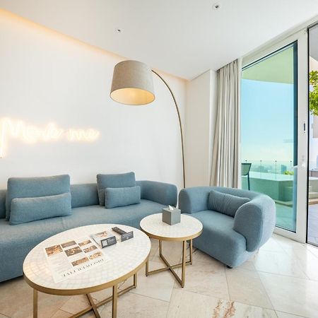 Five Jumeirah Village Dubai Exterior photo The photo shows a modern and stylish living space. It features a light blue sectional sofa and a matching armchair, creating a cozy seating area. Two round marble coffee tables are placed in front, one of which has some magazines or books on it. A ta