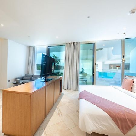 Five Jumeirah Village Dubai Exterior photo The photo shows a modern hotel room or a studio apartment. It features a large window with sheer curtains, allowing natural light to fill the space. There’s a double bed with a white bedspread and a light pink throw blanket at the foot. Opposite the 