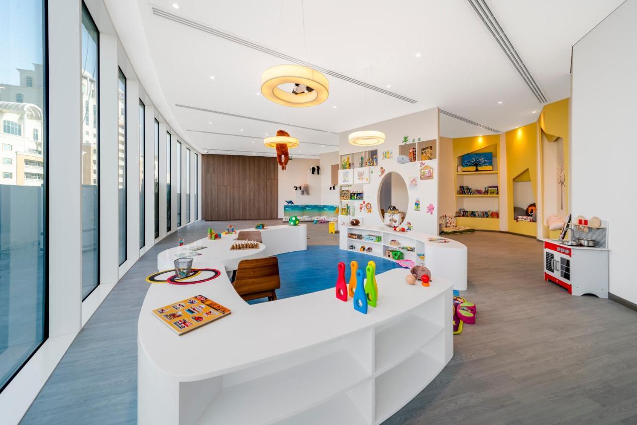 Five Jumeirah Village Dubai Exterior photo The photo depicts a bright and modern indoor play area designed for children. The space features large windows that allow natural light to flood in, creating a cheerful atmosphere. 

There are various play stations: one area has a rounded, low table 