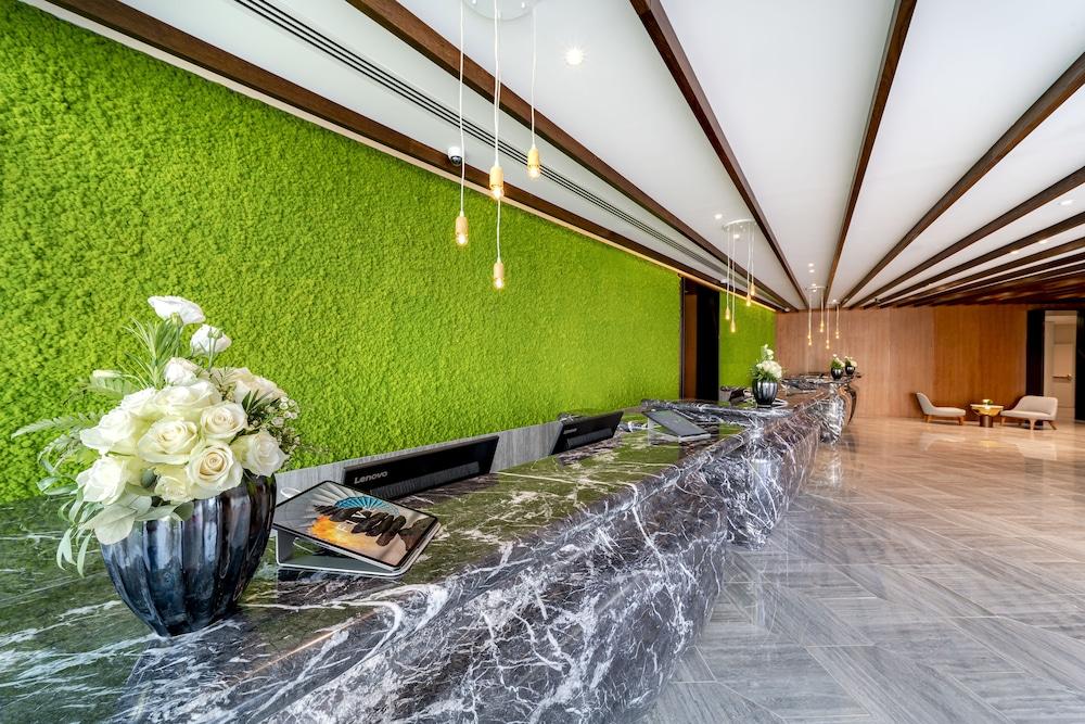 Five Jumeirah Village Dubai Exterior photo The photo shows a modern reception area of a building. The focal point is a long, marble reception desk that has a sleek, polished appearance. Behind the desk is a vibrant green wall that resembles moss or living greenery, adding a natural element to