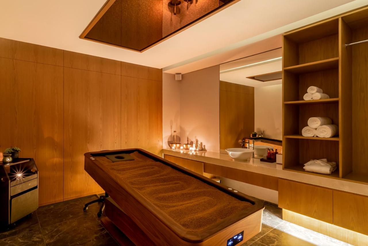 Five Jumeirah Village Dubai Exterior photo The photo shows a spa room designed for relaxation and wellness. It features a wooden treatment bed with a smooth, dark surface. The walls are made of warm wood paneling, creating a soothing environment. There is a large mirror on one wall, enhancing