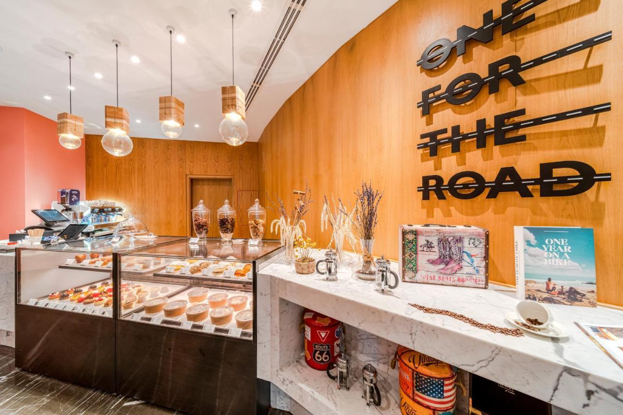 Five Jumeirah Village Dubai Exterior photo The image shows a stylish café or bakery interior. The wall is decorated with wooden paneling and features the phrase "ONE FOR THE ROAD" in large black letters. There is a display case filled with various pastries and desserts, showcasing a colorful 