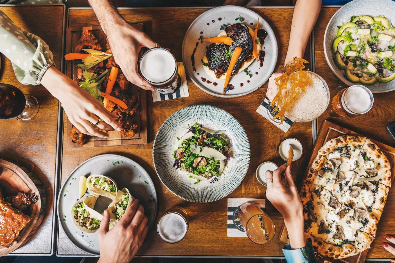 Five Jumeirah Village Dubai Exterior photo The photo displays a table filled with a variety of delicious food and drinks. There are several dishes, including a colorful salad in a round bowl, tacos, and what appears to be a pizza. On the side, there are also wooden platters with grilled veget