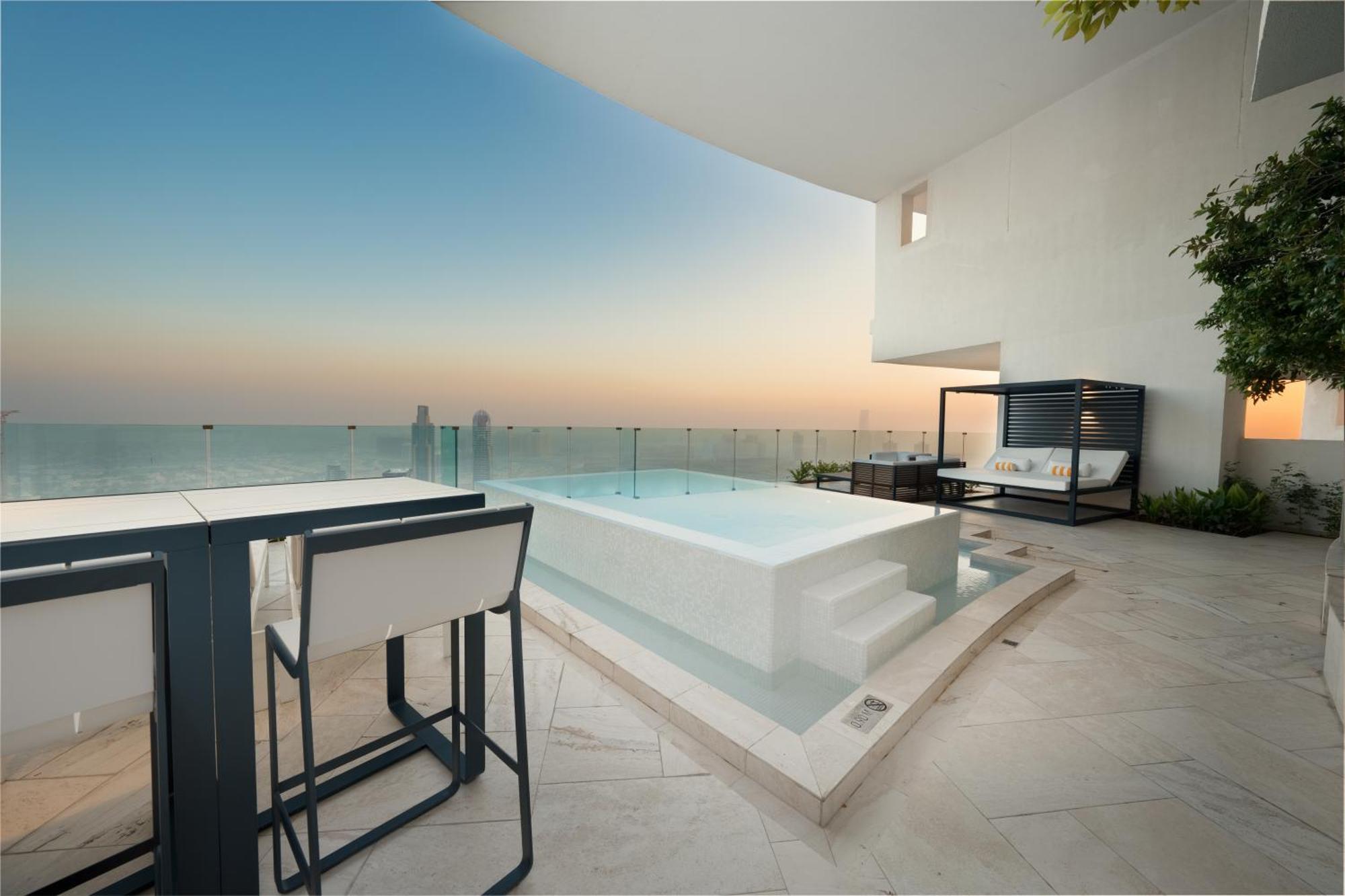 Five Jumeirah Village Dubai Exterior photo The photo depicts a luxurious outdoor space featuring a small infinity pool or hot tub that overlooks a scenic view. There is a stylish seating area nearby with modern furniture, including a table and chairs. The surroundings have a minimalist design