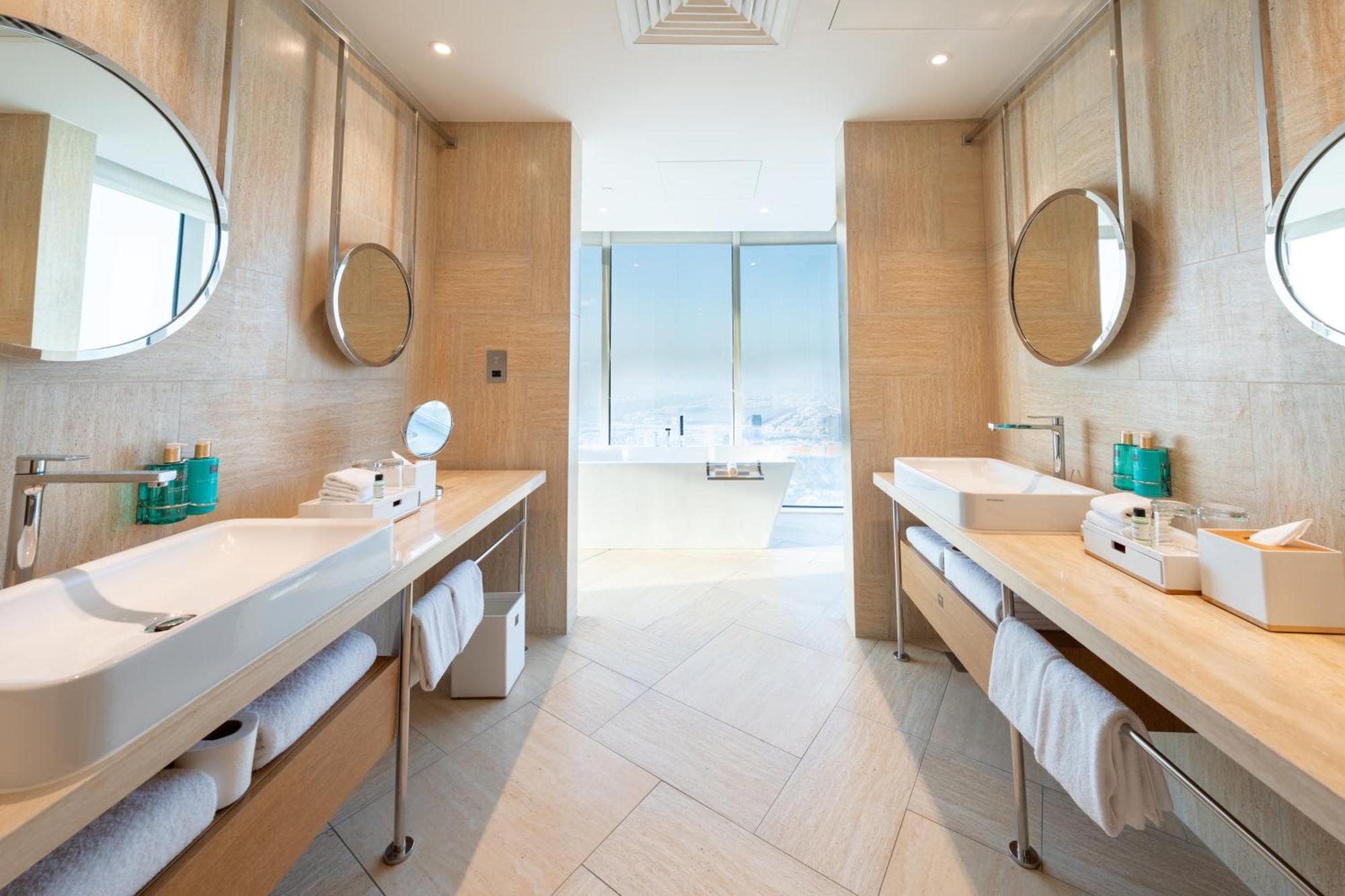 Five Jumeirah Village Dubai Exterior photo The photo shows a modern bathroom featuring two side-by-side vanities with circular mirrors above each sink. Each vanity has a white sink and a sleek wood countertop, with neatly rolled white towels stored underneath. The design is minimalistic, with