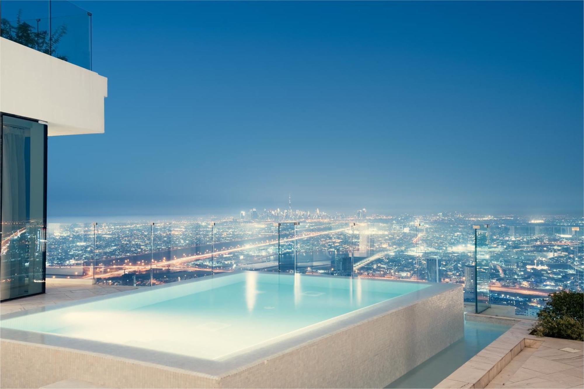 Five Jumeirah Village Dubai Exterior photo The photo showcases a luxurious infinity pool situated on an elevated terrace, overlooking a sprawling cityscape at night. The pool's water has a serene glow, reflecting the city lights below, which shimmer and create a vibrant backdrop. The architec