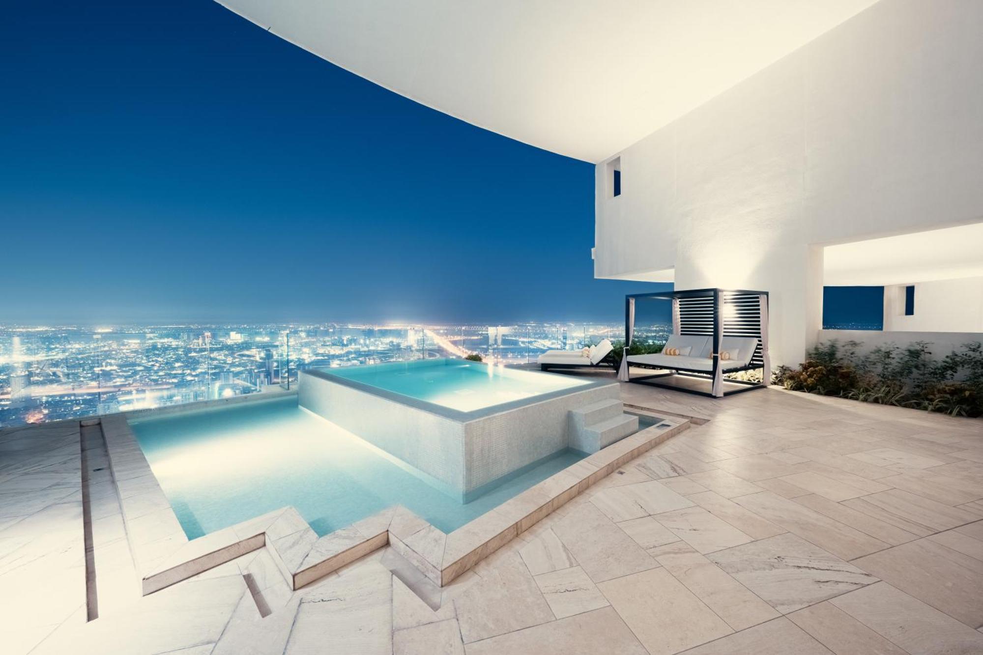 Five Jumeirah Village Dubai Exterior photo The photo showcases a luxurious outdoor space featuring a stylish infinity pool with a flowing design. The pool is illuminated and set against a backdrop of a sprawling city skyline at night, with twinkling lights from the buildings. There is a spaci