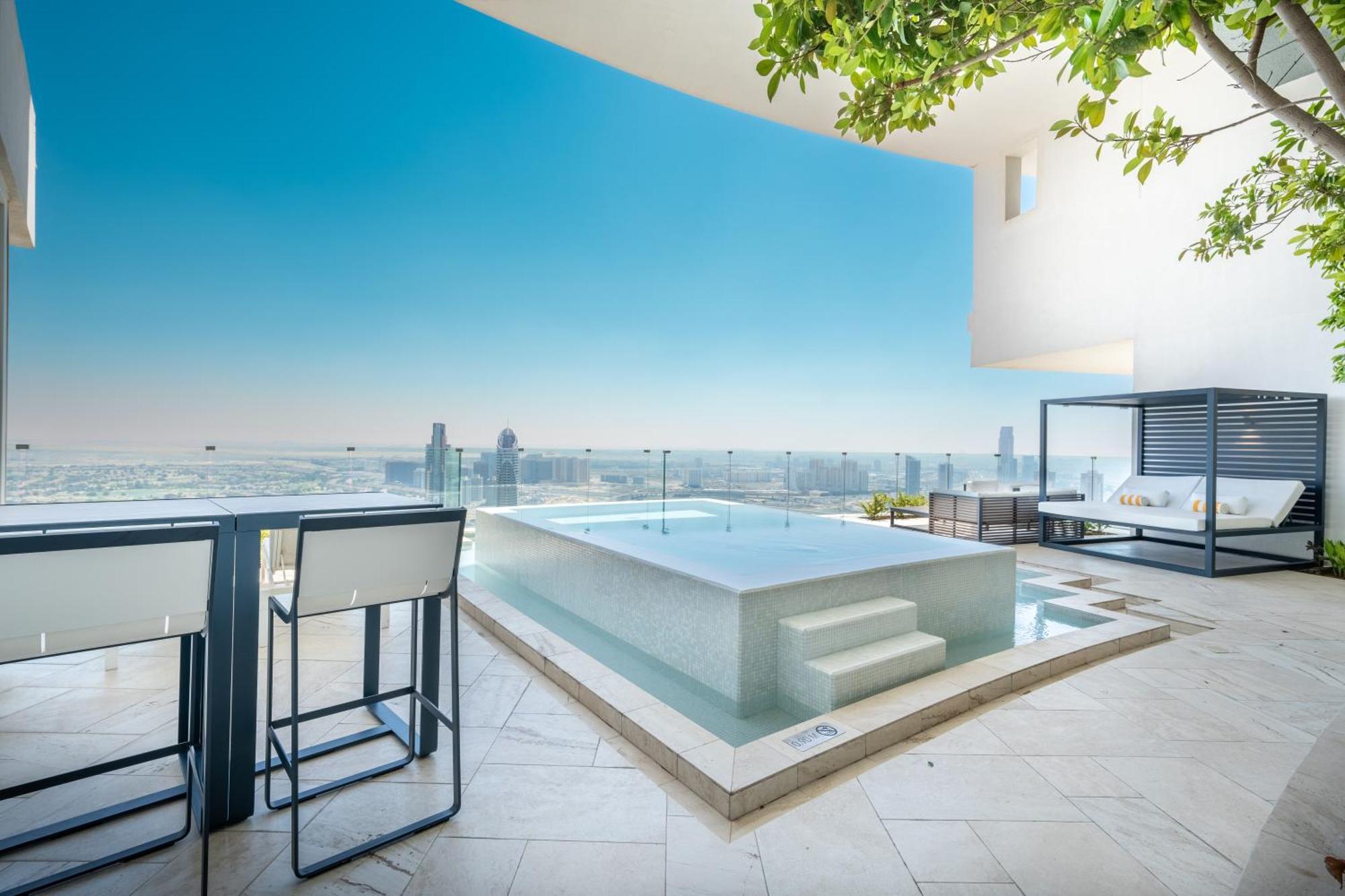 Five Jumeirah Village Dubai Exterior photo The photo shows a modern outdoor space featuring a sleek infinity pool. The pool appears to be situated on a terrace with a stunning view of a city skyline or landscape in the background. There are elegant lounge chairs and a shaded cabana area, crea