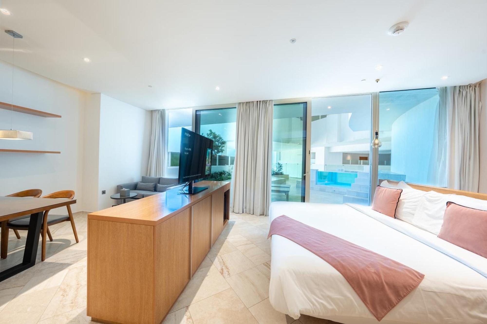 Five Jumeirah Village Dubai Exterior photo The photo shows a modern hotel room or a studio apartment. It features a large window with sheer curtains, allowing natural light to fill the space. There’s a double bed with a white bedspread and a light pink throw blanket at the foot. Opposite the 