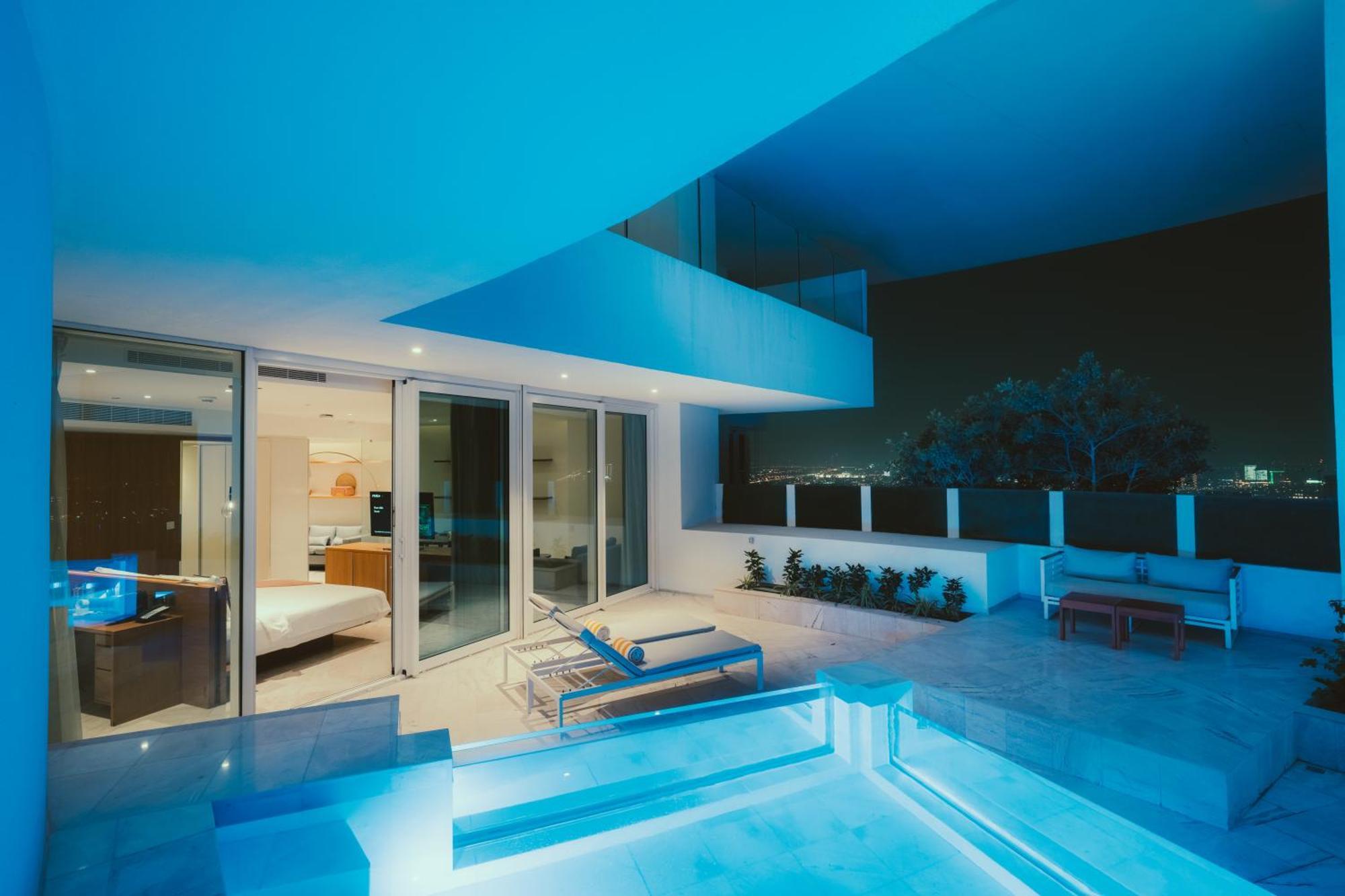 Five Jumeirah Village Dubai Exterior photo The photo depicts a modern architectural space at night. It features a stylish patio with a pool that has blue lighting, creating a serene ambiance. There are sleek lounge chairs beside the pool, and the interior of the building is visible through la