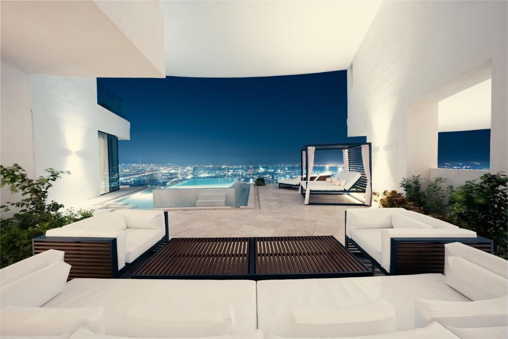 Five Jumeirah Village Dubai Exterior photo The photo depicts a stylish outdoor living space at night, featuring modern furniture. It includes a large sectional sofa with white cushions and a coffee table made of wood. In the background, there is a stunning view of a city illuminated at night,