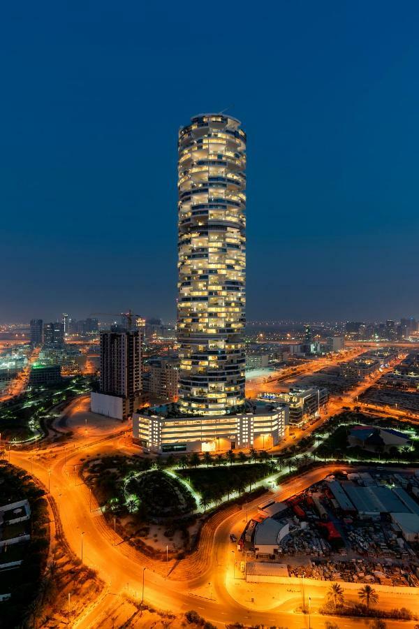 Five Jumeirah Village Dubai Exterior photo The photo shows a tall, modern skyscraper illuminated at night, surrounded by urban infrastructure. The building features a unique spiral design, with multiple floors visible and glowing lights in the windows. Below the tower, there are roads and oth