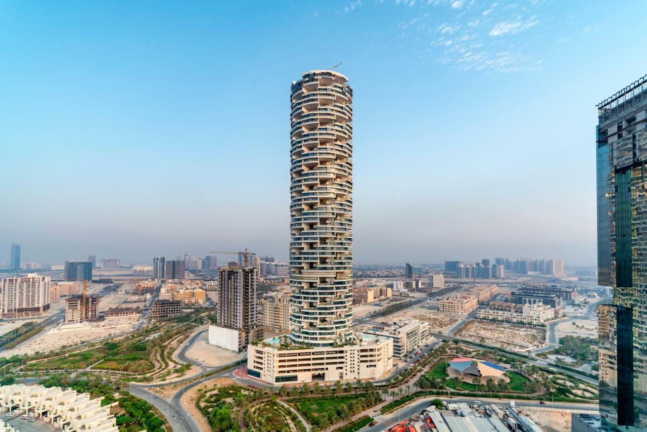 Five Jumeirah Village Dubai Exterior photo The photo shows a modern, twisting skyscraper set against a clear blue sky. The building features a unique, cylindrical shape with a series of balconies and terraces, giving it a distinctive appearance. Surrounding the tower are various other buildin