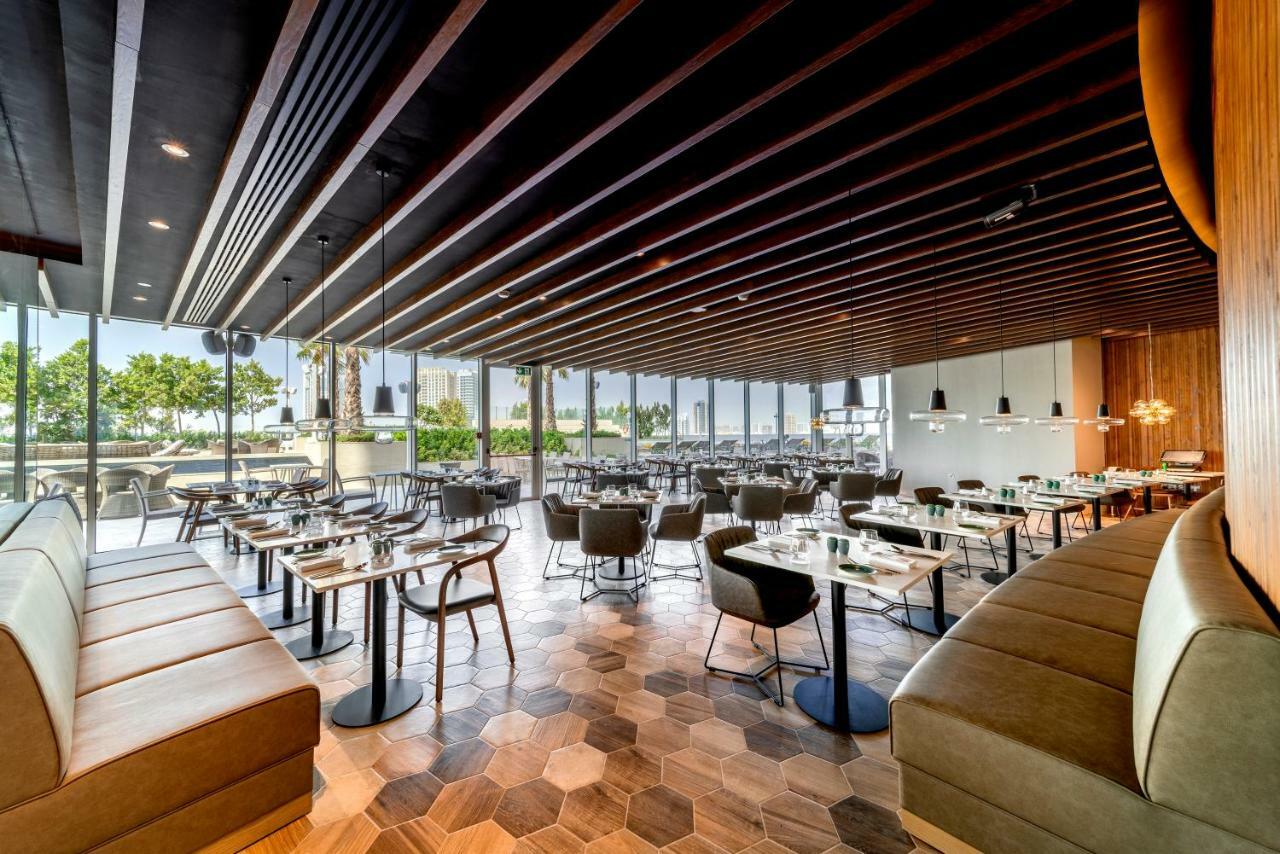 Five Jumeirah Village Dubai Exterior photo The photo shows the interior of a modern restaurant. It features a spacious layout with a combination of wooden and tiled flooring, characterized by hexagonal tiles. The ceiling has a modern design with wooden beams that add a sophisticated touch. Th