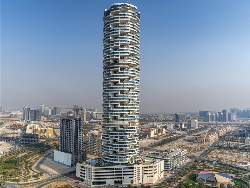 Five Jumeirah Village Dubai Exterior photo The photo shows a tall, modern skyscraper with a unique, twisting design. The building features numerous balconies and a stacked appearance, resembling a spiral or tower-like structure. Surrounding the skyscraper are other buildings and a sprawling u